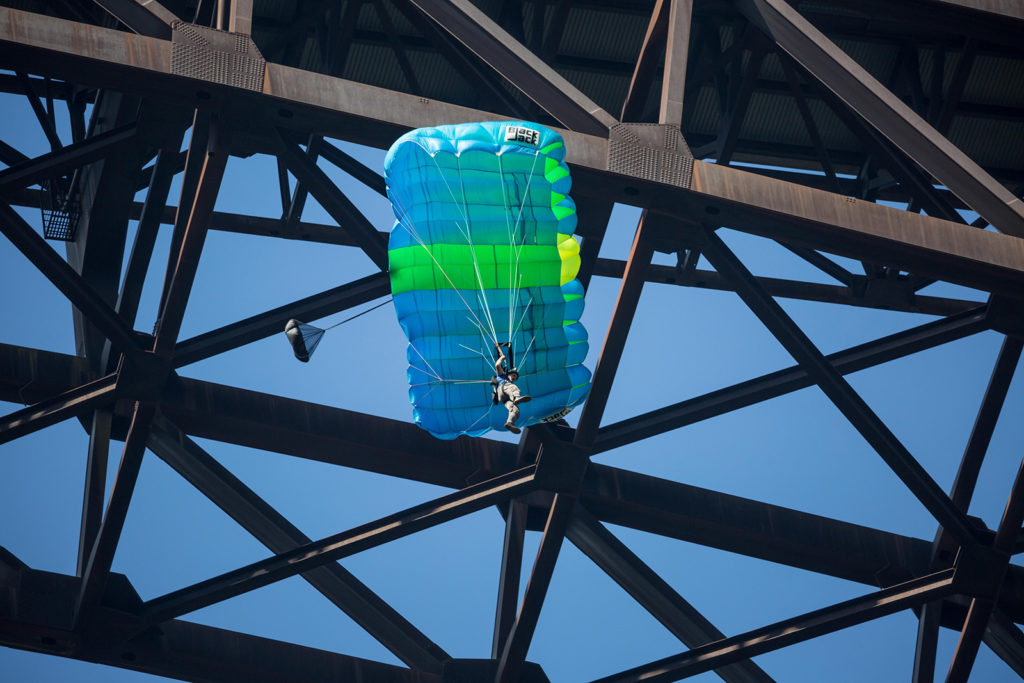 A low angle shot of a BASE jumper with a blue and green parachute jumping off of the new river gorge bridge on New River Gorge Bridge near Fayetteville, West Virginia