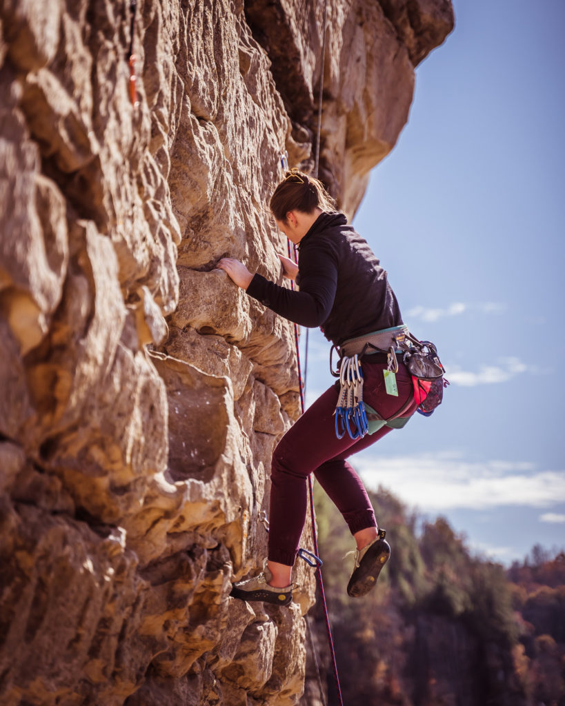 Woman in black rock climbing sandstone cliffs in new river gorge national park west virginia on a blue sky day
