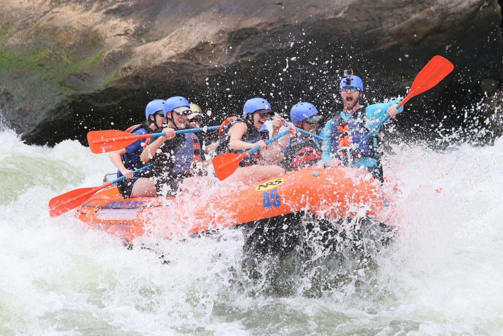 people dressed in blue white water rafting in an orange raft with rocks behind them new river gorge national park west virginia