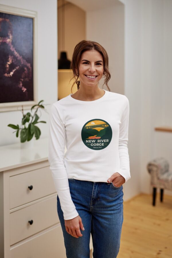 woman wearing a white long sleeve tshirt and jeans with new river gorge national park design on it with new river gorge bridge mountains and sunset