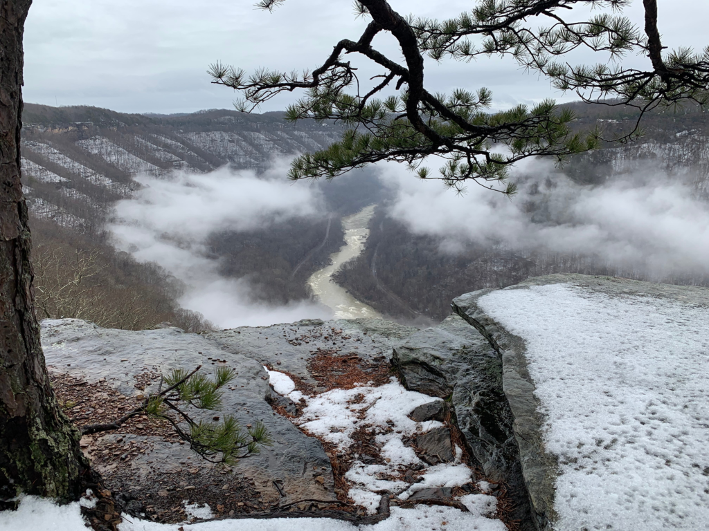 Breathtaking winter view of Diamond Point at Endless Wall, New River Gorge National Park. Snow-covered landscape with trees, cliffs, and the New River winding below.