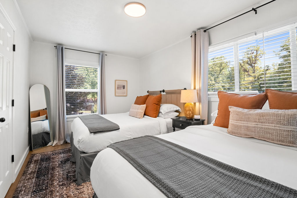 Gorge Getaway double queen bedroom with rust accent pillows, grey throws, and arch mirror
