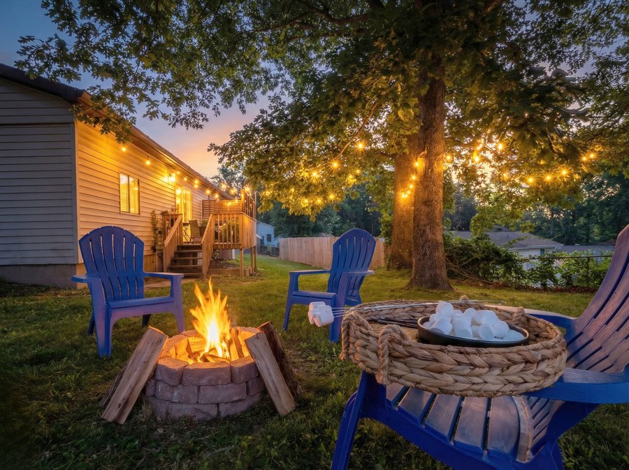 Blue Adirondack chairs around a firepit at dusk with string lights at the Delightful Gorge Getaway, Oak Hill WV